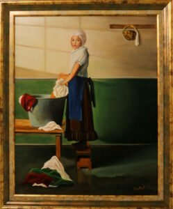 Cuadro que muestra a una niña con un vestido y un delantal sobre un taburete que lava la ropa en una palangana de metal sobre una mesa de madera. La niña mira al espectador. Al fondo hay una pared blanca y verde y la sombra de una ventana.